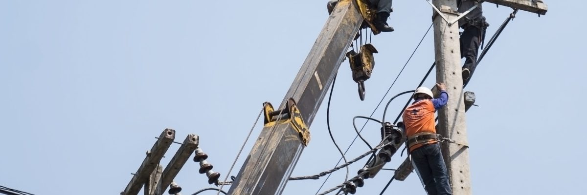 Insalubridade e periculosidade - eletricistas fixando a linha de transmissão de energia em um poste de eletricidade