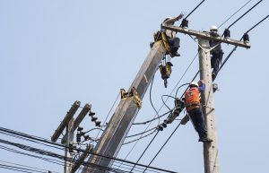 Insalubridade e periculosidade - eletricistas fixando a linha de transmissão de energia em um poste de eletricidade